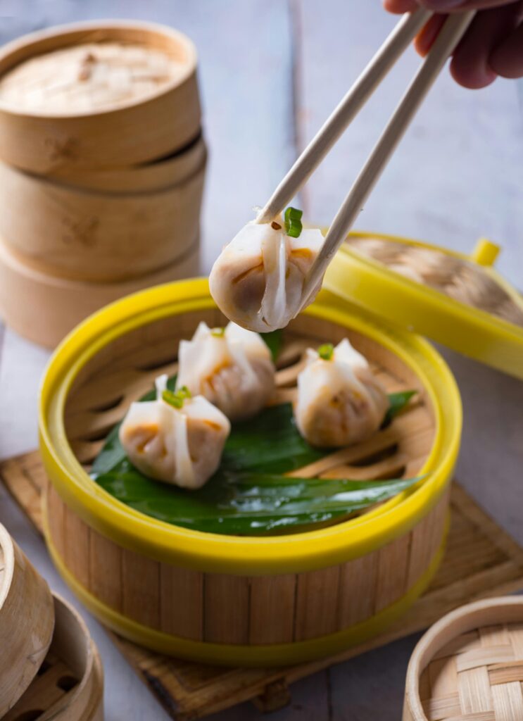 Close-up of tasty dim sum in a bamboo basket with chopsticks, perfect for Cantonese cuisine lovers.